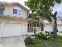 Exterior featuring light-toned horizontal siding, a single-car garage, covered entry porch, established front landscaping, and a prominent mature tree - #48 6608 158 Av Nw, Edmonton, AB  - Outdoor With Deck Patio Veranda 