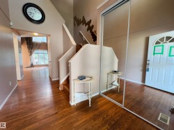 Entryway featuring wood-finish flooring, a white paneled front door with an arched transom, and a mirrored closet door - 