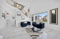 Bright open-concept living area featuring a double-height ceiling, large picture windows, and a contemporary open-riser staircase with a gold-tone railing - 