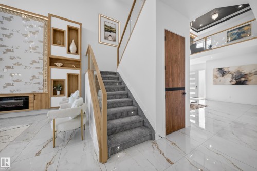 Double-height entryway featuring a modern staircase with glass railing and wood-finish handrail, alongside white and gold veined porcelain tile flooring - 423 Robinson Bv, Leduc, AB - Indoor Photo Showing Other Room
