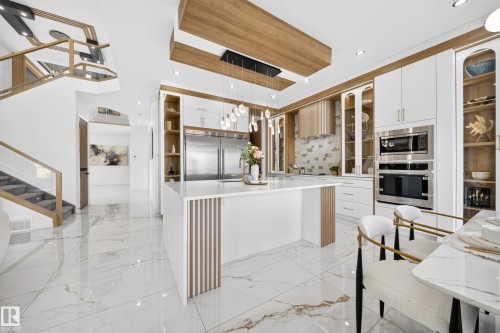 Gourmet kitchen featuring a waterfall island, integrated stainless steel appliances, extensive cabinetry with glass display fronts, recessed lighting, and wood-finish ceiling accents - 423 Robinson Bv, Leduc, AB - Indoor Photo Showing Kitchen