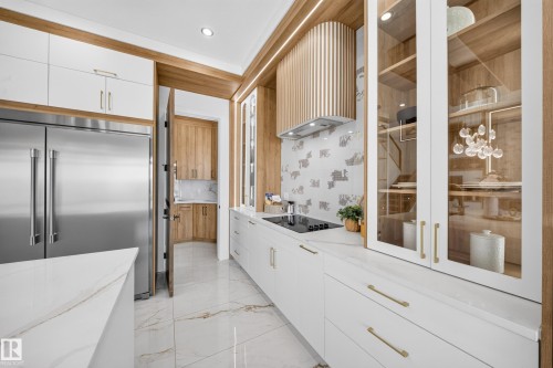 Gourmet kitchen featuring a built-in stainless steel refrigerator, integrated cooktop, marble-look countertops, white cabinetry with gold-tone hardware, and a wood-slat range hood - 423 Robinson Bv, Leduc, AB - Indoor Photo Showing Kitchen