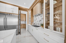 Gourmet kitchen featuring a built-in stainless steel refrigerator, integrated cooktop, marble-look countertops, white cabinetry with gold-tone hardware, and a wood-slat range hood - 