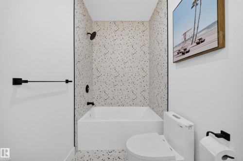 Bathroom featuring a white soaking tub with black fixtures, speckled wall tile extending to the floor, and a modern toilet - 423 Robinson Bv, Leduc, AB - Indoor Photo Showing Bathroom