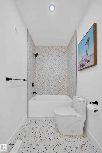 Bathroom featuring a white bathtub, black shower fixtures, a toilet, and patterned terrazzo-style flooring - 423 Robinson Bv, Leduc, AB - Indoor Photo Showing Bathroom