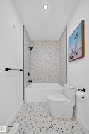 Bathroom featuring a white bathtub, black shower fixtures, a toilet, and patterned terrazzo-style flooring - 