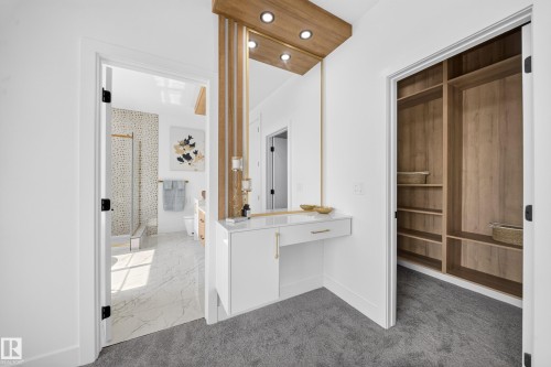 Dedicated vanity area with integrated lighting, a built-in closet with custom shelving, and an adjacent bathroom featuring a glass-enclosed shower, light-toned tile flooring, and a contemporary vanity with a contrasting wood finish - 423 Robinson Bv, Leduc, AB - Indoor