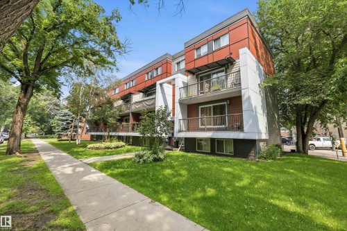 Multi-story building featuring modern red and gray paneling, private balconies with metal railings, and a concrete sidewalk bordering a manicured lawn - #8 10931 83 St Nw, Edmonton, AB - Outdoor With Balcony