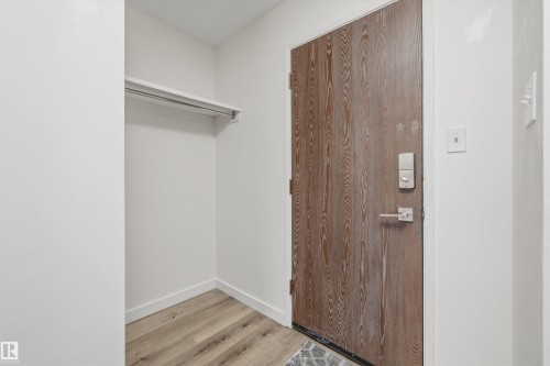 Entry area featuring wood-finish flooring, a contemporary wooden door with modern hardware, and a built-in closet with a hanging rod - #8 10931 83 St Nw, Edmonton, AB - Indoor