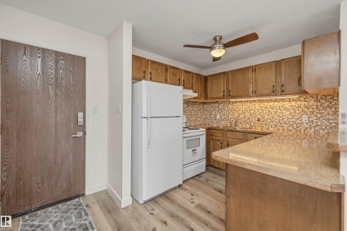 Kitchen featuring wood-finish cabinetry, mosaic tile backsplash, and light-toned countertops - #8 10931 83 St Nw, Edmonton, AB - Indoor Photo Showing Kitchen