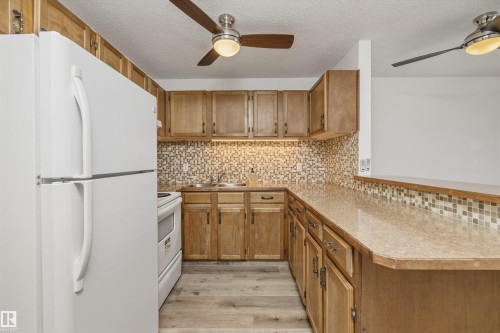 Kitchen featuring a built-in breakfast bar, wood-finish cabinetry, and a mosaic tile backsplash - #8 10931 83 St Nw, Edmonton, AB - Indoor Photo Showing Kitchen