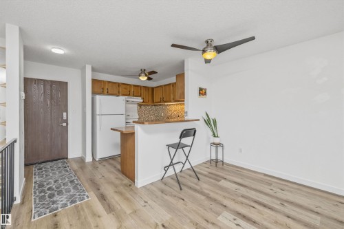 Open-concept living space featuring wood-finish flooring, a kitchen with wood cabinetry and white appliances, and a breakfast bar - #8 10931 83 St Nw, Edmonton, AB - Indoor Photo Showing Kitchen