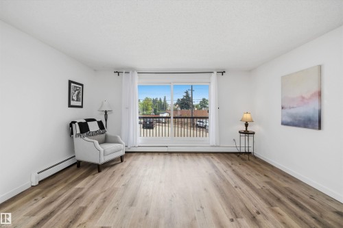 Spacious room featuring wood-finish flooring and a large window with a black railing - #8 10931 83 St Nw, Edmonton, AB - Indoor Photo Showing Living Room
