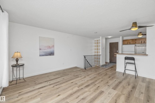 Open-concept living area featuring wood-finish flooring, white walls, and a prominent ceiling fan with integrated lighting - #8 10931 83 St Nw, Edmonton, AB - Indoor