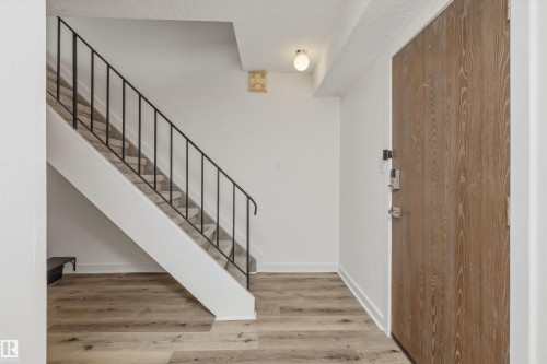 Lower level Entryway featuring wood-finish flooring, a carpeted staircase with a black metal railing, a flush mount ceiling light, and a wood-finish entry door with modern hardware - #8 10931 83 St Nw, Edmonton, AB - Indoor Photo Showing Other Room