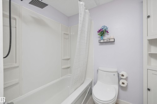 Bathroom featuring a white tub/shower combination with a rainfall showerhead, and a white commode - #8 10931 83 St Nw, Edmonton, AB - Indoor Photo Showing Bathroom