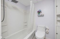 Bathroom featuring a white tub/shower combination with a rainfall showerhead, and a white commode - 