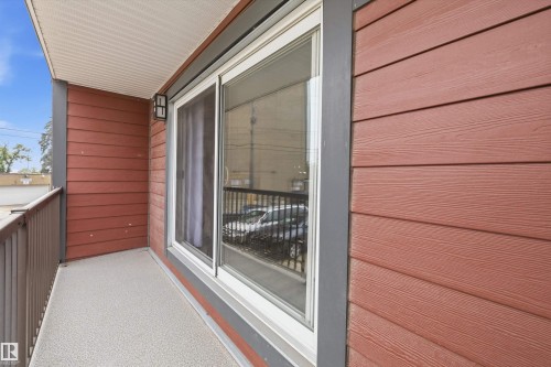 Private balcony with textured flooring, framed by horizontal wood-finish siding and a modern exterior light fixture - #8 10931 83 St Nw, Edmonton, AB - Outdoor With Balcony With Exterior
