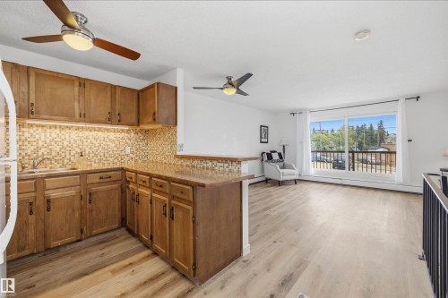 Open-concept living space featuring wood-finish flooring, a kitchen with wood cabinetry and mosaic tile backsplash, and a spacious balcony with black railings - #8 10931 83 St Nw, Edmonton, AB - Indoor Photo Showing Other Room