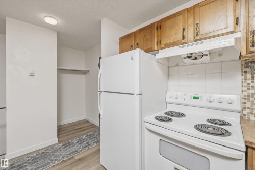 Kitchen featuring wood-finish cabinetry, white tile backsplash, and a white electric range with an overhead vent - #8 10931 83 St Nw, Edmonton, AB - Indoor Photo Showing Kitchen