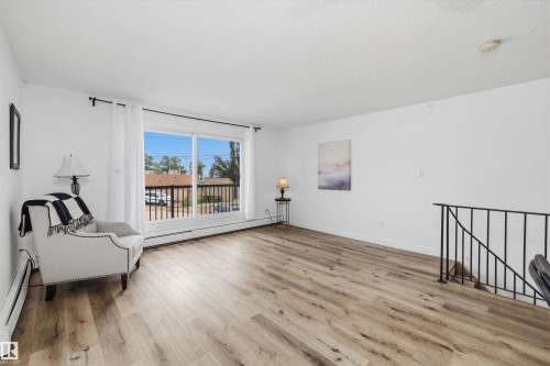 Spacious living area featuring light wood-finish flooring, white walls, and a large sliding glass door with a balcony - #8 10931 83 St Nw, Edmonton, AB - Indoor Photo Showing Living Room