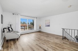 Spacious living area featuring light wood-finish flooring, white walls, and a large sliding glass door with a balcony - 