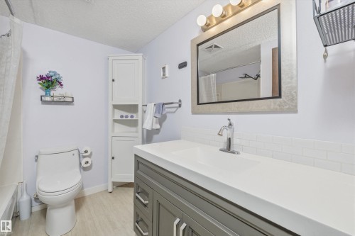 Contemporary bathroom featuring a single vanity with integrated sink, white subway tile backsplash, and a framed mirror with an overhead light fixture - #8 10931 83 St Nw, Edmonton, AB - Indoor Photo Showing Bathroom