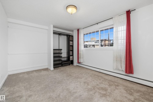 Carpeted room featuring a white ceiling and walls, a window with horizontal panes, an open closet system with shelving, and a semi-flush mount ceiling light - #8 10931 83 St Nw, Edmonton, AB - Indoor Photo Showing Other Room
