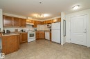 Open-concept kitchen featuring wood-finish cabinetry, white appliances, and a durable tiled floor - #6201 7331 South Terwillegar Dr Nw, Edmonton, AB  - Indoor Photo Showing Kitchen With Double Sink 