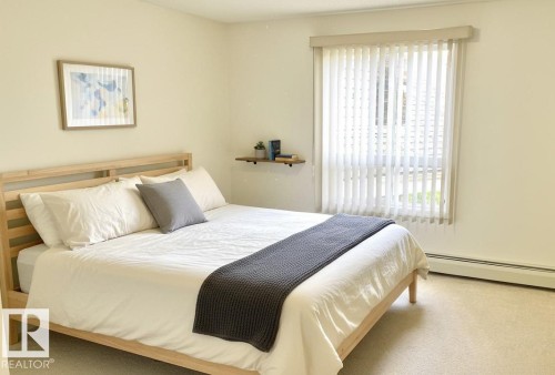 Carpeted room with a large window featuring vertical blinds, a wall-mounted shelf, and a baseboard radiator - #6201 7331 South Terwillegar Dr Nw, Edmonton, AB - Indoor Photo Showing Bedroom