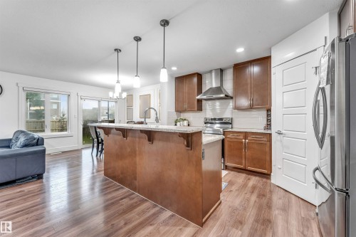 Open-concept kitchen featuring an island with a breakfast bar, recessed lighting, wood-finish flooring, and stainless steel appliances - 6727 20 Ave Sw, Edmonton, AB - Indoor Photo Showing Kitchen With Upgraded Kitchen