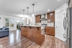Open-concept kitchen featuring an island with a breakfast bar, recessed lighting, wood-finish flooring, and stainless steel appliances - 