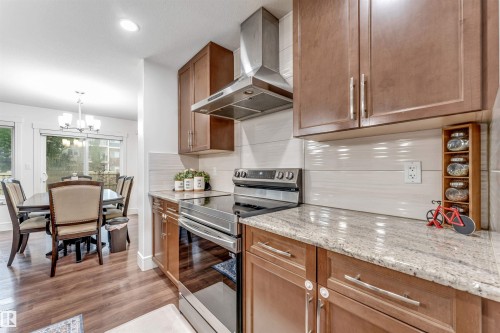 Kitchen featuring wood-finish flooring, light-toned cabinetry, stainless steel appliances, granite countertops, and a tile backsplash - 6727 20 Ave Sw, Edmonton, AB - Indoor Photo Showing Kitchen