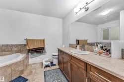 Spacious bathroom featuring a built-in soaking tub with tiled surround, a large vanity with ample countertop space, an integrated sink, and wood-finish cabinetry - 