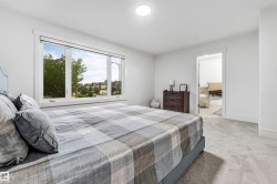 Expansive bedroom featuring light gray carpeting, a large picture window, and a white framed doorway opening to a bathroom with tiled flooring - 
