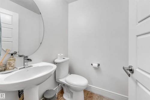 Pedestal sink with chrome faucet, circular mirror, and white paneled door - 6727 20 Ave Sw, Edmonton, AB - Indoor Photo Showing Bathroom