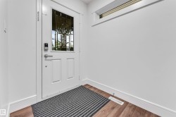 Welcoming entryway featuring a white six-panel door with decorative glass insert, polished chrome hardware, and mixed flooring including wood-finish planks and a striped entry mat - 