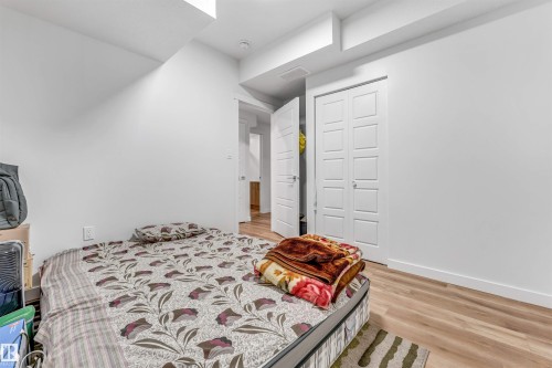 Bedroom featuring light wood-finish flooring, white walls, white baseboards, and bi-fold closet doors with panel detailing - 6727 20 Ave Sw, Edmonton, AB - Indoor Photo Showing Bedroom