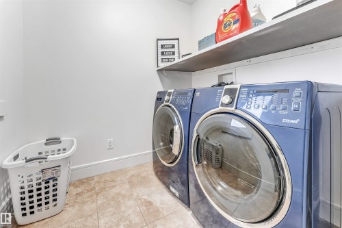 Dedicated laundry area featuring a front-loading washer and dryer set, neutral-toned floor tiling, white walls, and a built-in overhead shelving unit - 6727 20 Ave Sw, Edmonton, AB - Indoor Photo Showing Laundry Room