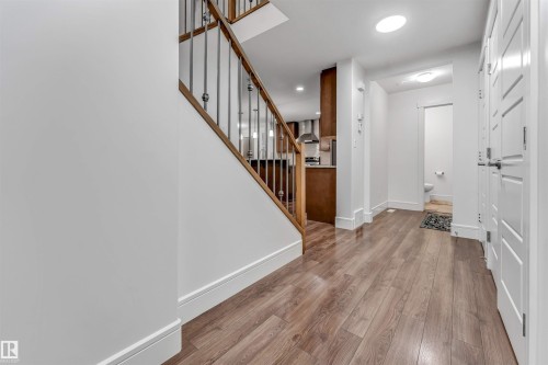 Entryway featuring wood-finish flooring, white baseboards, and a wooden staircase with iron balusters - 6727 20 Ave Sw, Edmonton, AB - Indoor Photo Showing Other Room