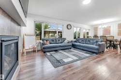 Open-concept living area featuring wood-finish flooring, a tiled fireplace surround, and multiple windows - 