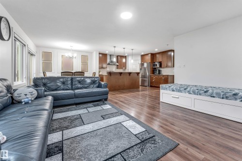 Open-concept living space featuring wood-finish flooring, recessed lighting, a dining area with a chandelier, a kitchen with wood cabinetry and stainless steel appliances, and a built-in storage bench - 6727 20 Ave Sw, Edmonton, AB - Indoor Photo Showing Living Room
