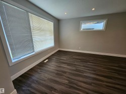 Spacious room featuring wood-finish flooring, two large windows with blinds, recessed ceiling lighting, and neutral wall paint - 