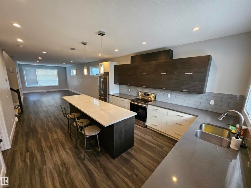Modern kitchen featuring an expansive island with seating, dark wood-finish cabinetry, and stainless steel appliances - 9311 66 Avenue Nw, Edmonton, AB - Indoor Photo Showing Kitchen With Double Sink