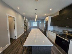 Modern kitchen featuring a large island with white countertop, dark wood-finish cabinetry, stainless steel appliances, and wood-finish flooring - 