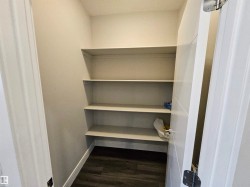 Pantry featuring multiple built-in shelving units, light-toned walls, and wood-finish flooring - 