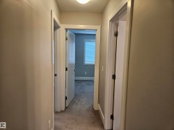 Interior hallway featuring neutral wall paint, white trim, and a textured ceiling - 