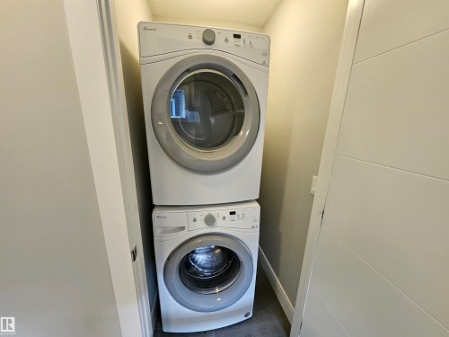 Stackable white washer and dryer units within a dedicated laundry alcove, featuring a paneled door - 9311 66 Avenue Nw, Edmonton, AB - Indoor Photo Showing Laundry Room