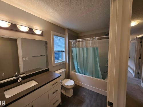 Bathroom featuring a vanity with a rectangular sink and dark countertop, a toilet, a bathtub with shower, wood-finish flooring, and a window with blinds - 9311 66 Avenue Nw, Edmonton, AB - Indoor Photo Showing Bathroom