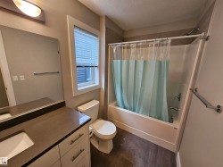 Bathroom featuring a vanity with an integrated sink, a large mirror, a window with blinds, a toilet, and a combined shower and bathtub with tile surround - 